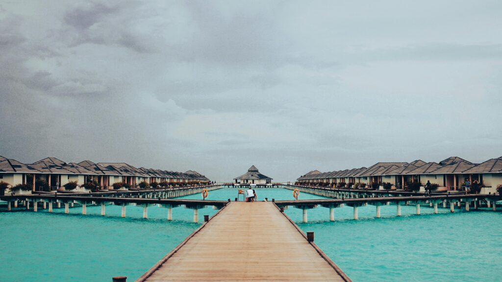 Scenic view of wooden pathway leading to overwater villas in Maldives on a cloudy day.